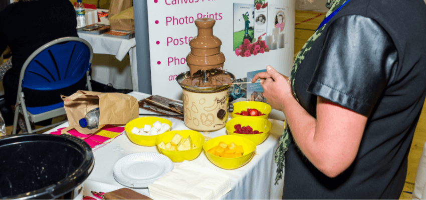 a person standing next to a business expo stand with a chocolate fountain and fruit on it